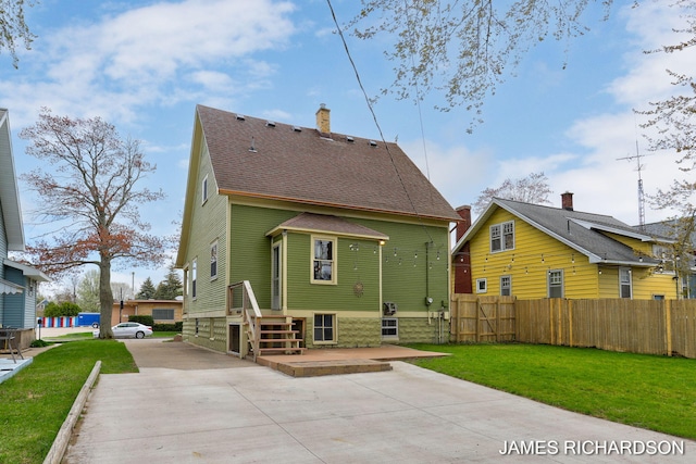 back of property with fence, concrete driveway, a yard, and a shingled roof
