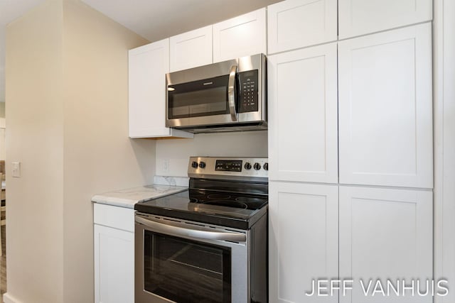 kitchen with light stone counters, appliances with stainless steel finishes, and white cabinets