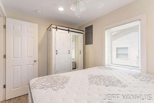 bedroom with a barn door, light wood-style flooring, a ceiling fan, recessed lighting, and electric panel
