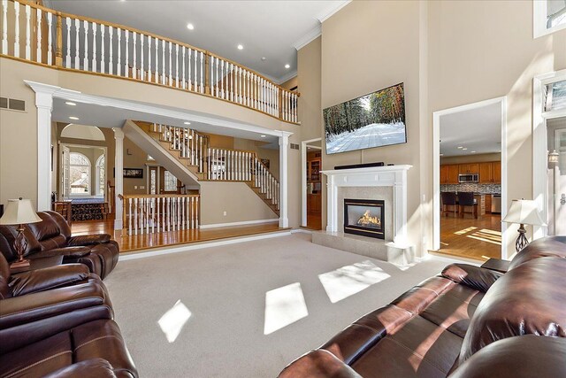 carpeted living area with a premium fireplace, stairs, decorative columns, a towering ceiling, and visible vents