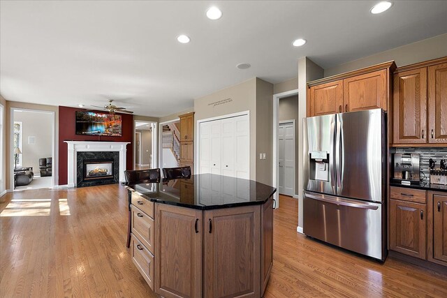 kitchen with ceiling fan, stainless steel fridge, a premium fireplace, light wood-type flooring, and a kitchen island