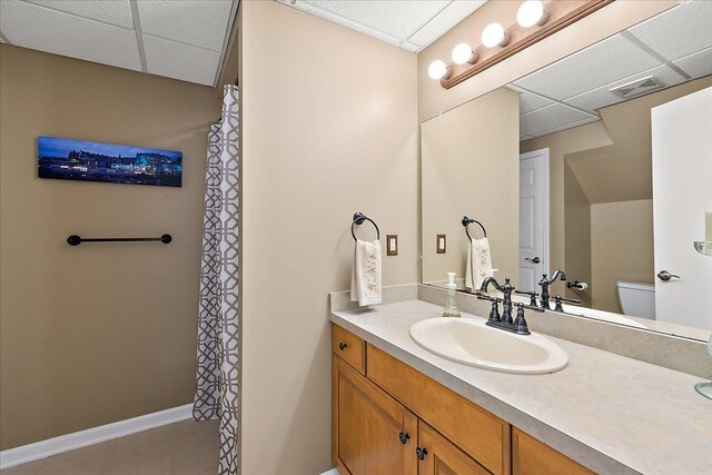 bathroom featuring vanity, baseboards, a drop ceiling, and toilet