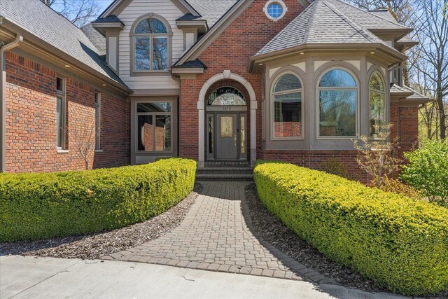 doorway to property with brick siding and roof with shingles