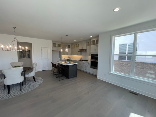 kitchen featuring a kitchen breakfast bar, a chandelier, wood finished floors, gas stovetop, and a center island with sink