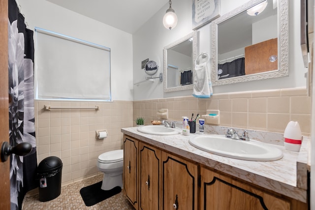 full bathroom featuring toilet, double vanity, tile walls, tile patterned flooring, and a wainscoted wall