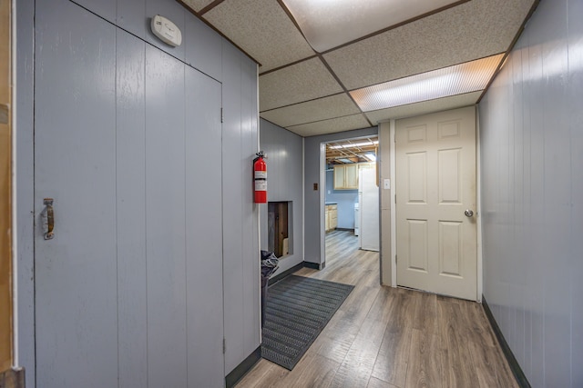 corridor with light wood-type flooring and a drop ceiling
