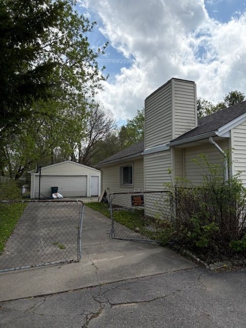 view of side of property featuring a detached garage, fence, a chimney, and an outdoor structure