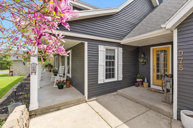 view of exterior entry featuring a porch and roof with shingles