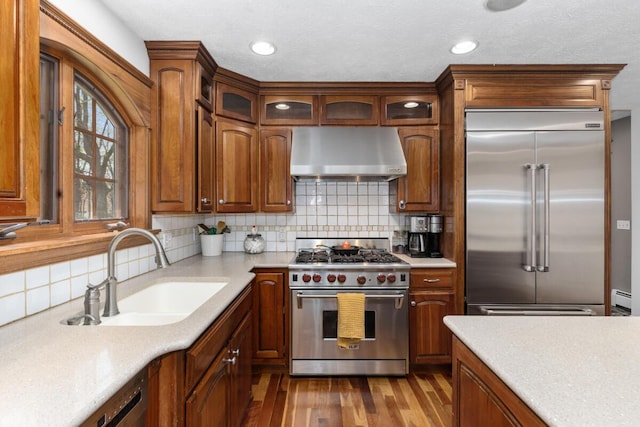 kitchen with range hood, hardwood / wood-style flooring, a sink, light countertops, and premium appliances