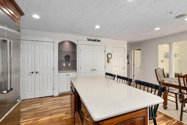kitchen with a kitchen island, light wood-style floors, light countertops, a textured ceiling, and stainless steel built in fridge