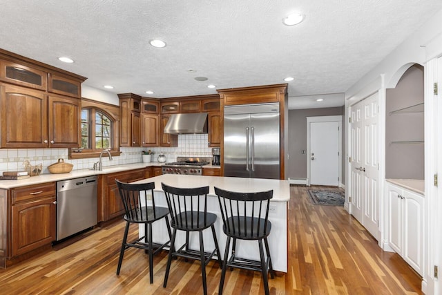kitchen with appliances with stainless steel finishes, a sink, a baseboard heating unit, a breakfast bar, and under cabinet range hood