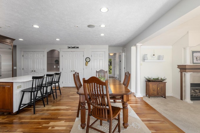 dining space with a textured ceiling, recessed lighting, baseboards, light wood-style floors, and ornate columns