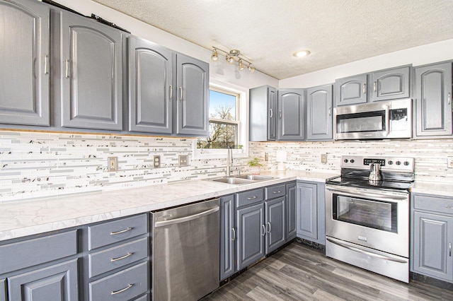 kitchen featuring gray cabinets, a textured ceiling, dark wood finished floors, a sink, and stainless steel appliances