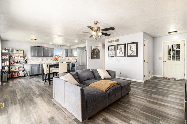 living room featuring a ceiling fan, a textured ceiling, visible vents, dark wood finished floors, and baseboards