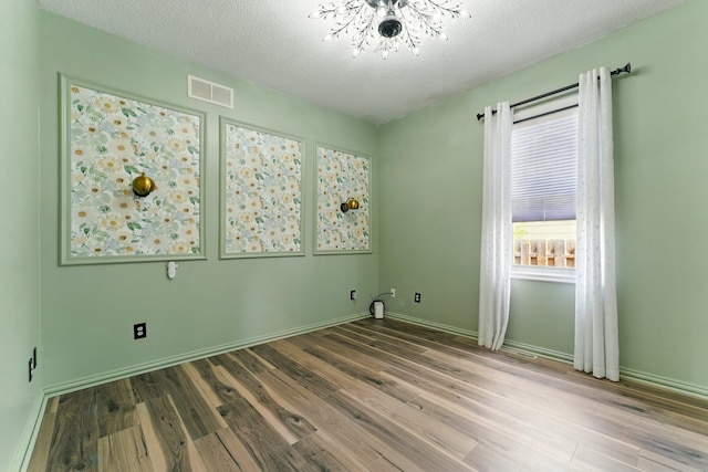 empty room featuring visible vents, baseboards, a textured ceiling, and wood finished floors