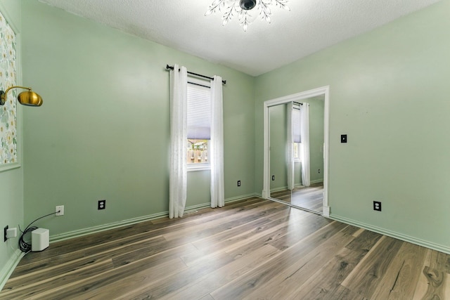 unfurnished bedroom with a textured ceiling, baseboards, an inviting chandelier, and wood finished floors