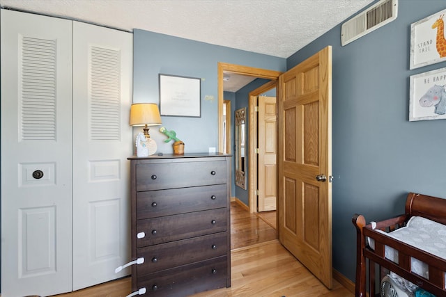 bedroom featuring a textured ceiling, visible vents, baseboards, a closet, and light wood-style floors