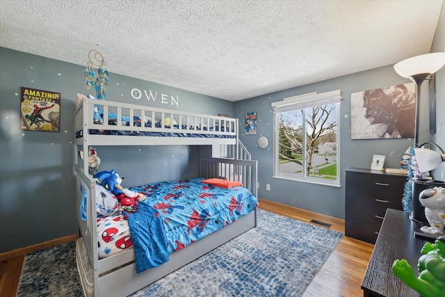 bedroom featuring baseboards, a textured ceiling, visible vents, and wood finished floors