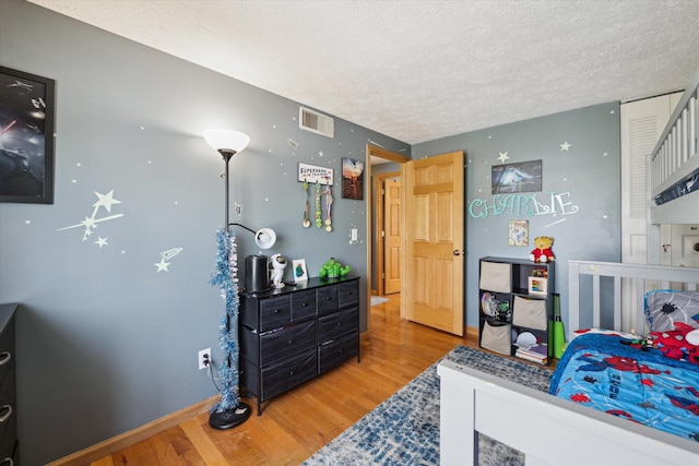 bedroom featuring baseboards, a textured ceiling, visible vents, and wood finished floors