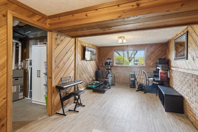 exercise room with wood walls, a textured ceiling, wood finished floors, and brick wall