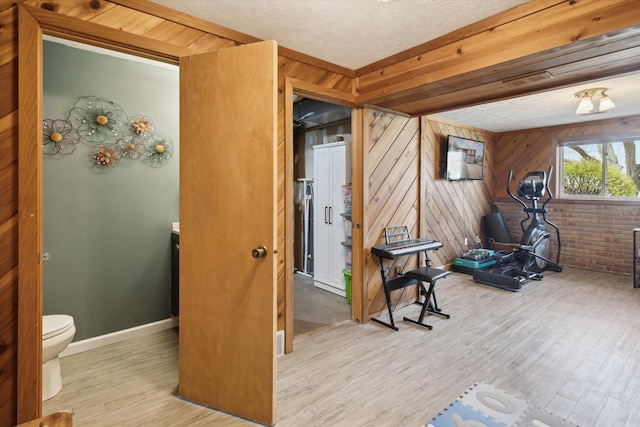 workout room with baseboards, wood walls, a textured ceiling, and wood finished floors