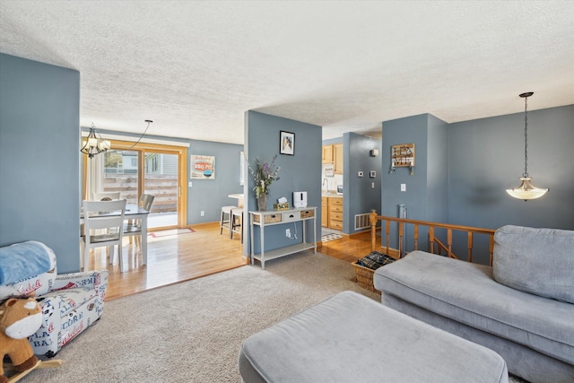 carpeted living area featuring a textured ceiling, visible vents, wood finished floors, baseboards, and a notable chandelier