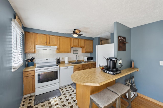 kitchen with white appliances, under cabinet range hood, a sink, and light countertops