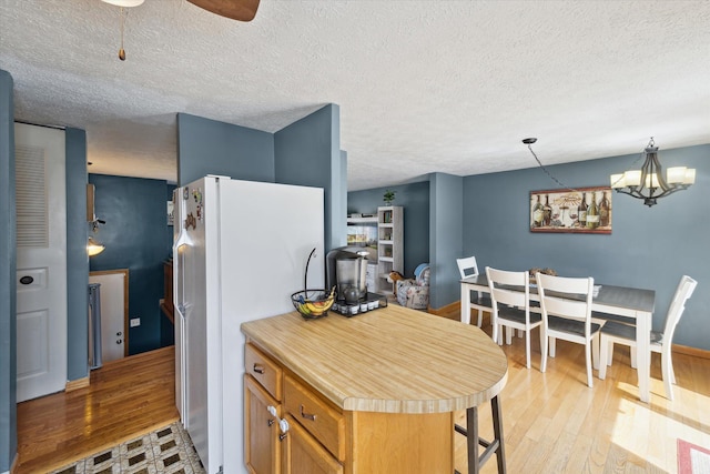 kitchen with brown cabinetry, a textured ceiling, light countertops, freestanding refrigerator, and light wood-style floors