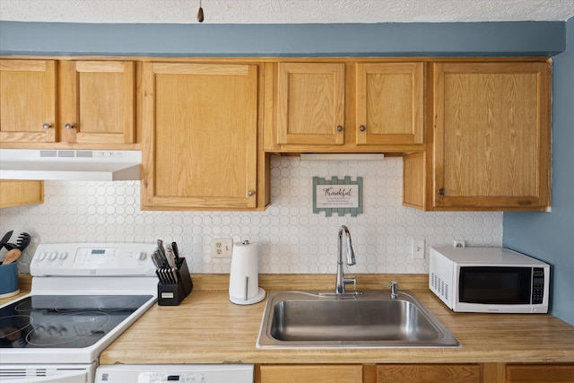 kitchen featuring white appliances, light countertops, under cabinet range hood, a sink, and backsplash