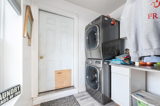 clothes washing area featuring baseboards, stacked washer and dryer, and cabinet space