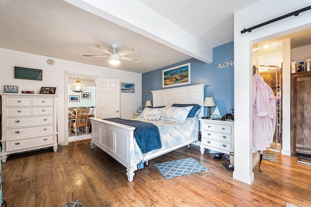 bedroom with beamed ceiling, ceiling fan, a barn door, and wood finished floors