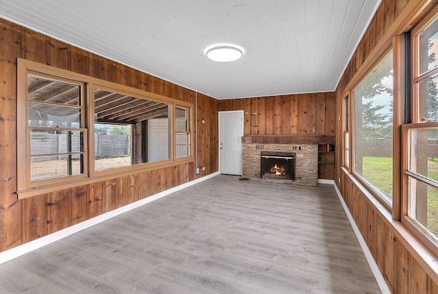 unfurnished living room with a brick fireplace, wood finished floors, wooden walls, and a wealth of natural light