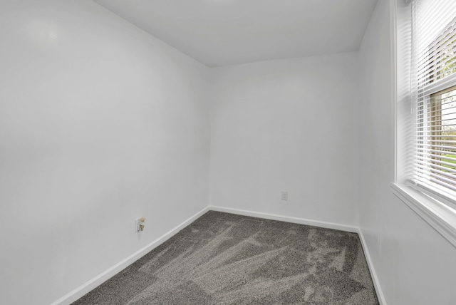 unfurnished room with baseboards and dark carpet
