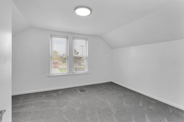 additional living space with baseboards, vaulted ceiling, dark carpet, and visible vents