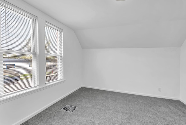 additional living space featuring baseboards, visible vents, dark carpet, and lofted ceiling