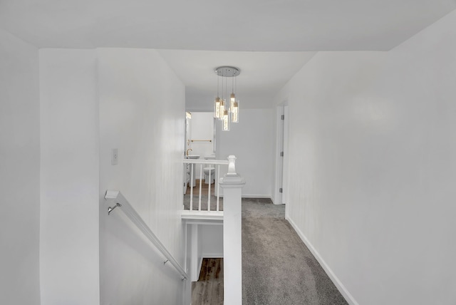 hall featuring carpet flooring, baseboards, and an upstairs landing