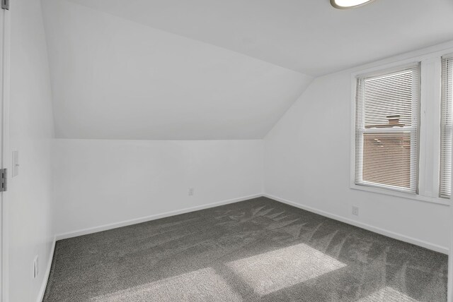 bonus room featuring baseboards, vaulted ceiling, and dark carpet