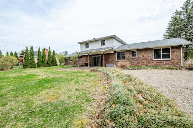 back of house with a yard, brick siding, fence, and roof with shingles