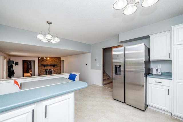 kitchen featuring pendant lighting, a brick fireplace, white cabinets, a chandelier, and stainless steel fridge