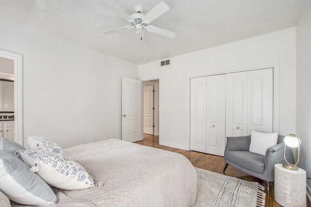 bedroom with a ceiling fan, visible vents, wood finished floors, baseboards, and a closet