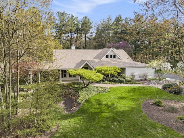 view of front facade with a chimney, roof with shingles, and a front lawn