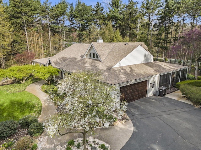 view of front facade featuring roof with shingles, a garage, a sunroom, a chimney, and driveway