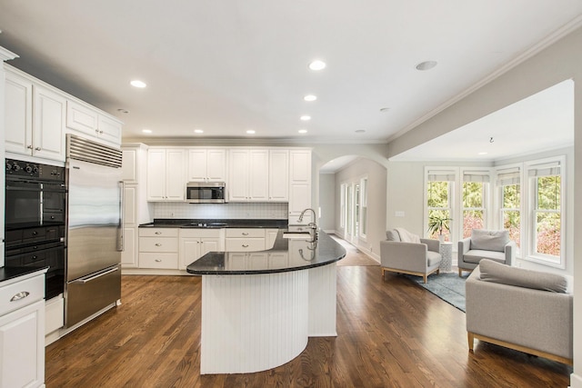 kitchen featuring crown molding, dark countertops, open floor plan, arched walkways, and appliances with stainless steel finishes