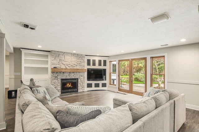 living area with visible vents, a stone fireplace, recessed lighting, a wainscoted wall, and dark wood finished floors