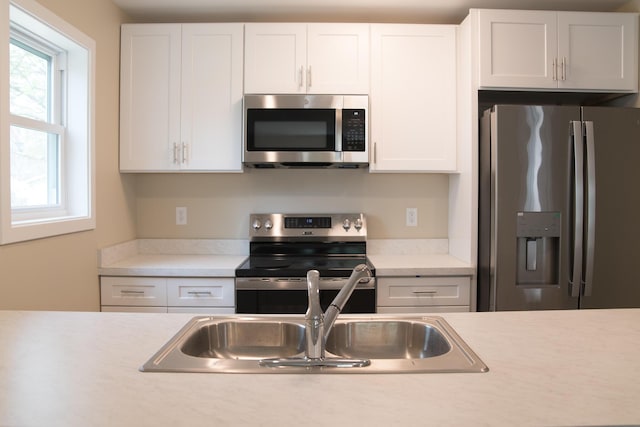 kitchen featuring light countertops, stainless steel appliances, white cabinetry, and a sink