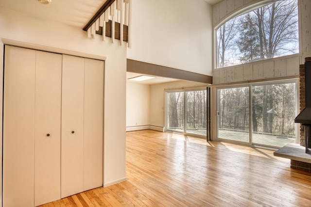 unfurnished living room with plenty of natural light, baseboard heating, light wood-style flooring, and a towering ceiling