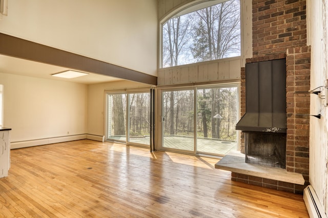 unfurnished living room with wood finished floors, a towering ceiling, a baseboard heating unit, and a fireplace