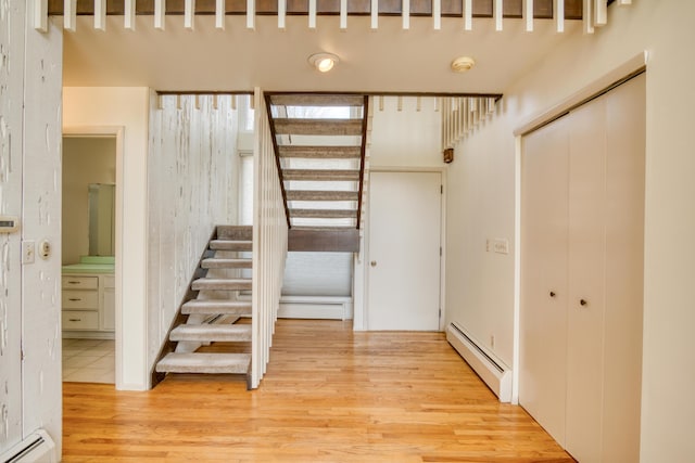 stairway with a baseboard heating unit and wood finished floors