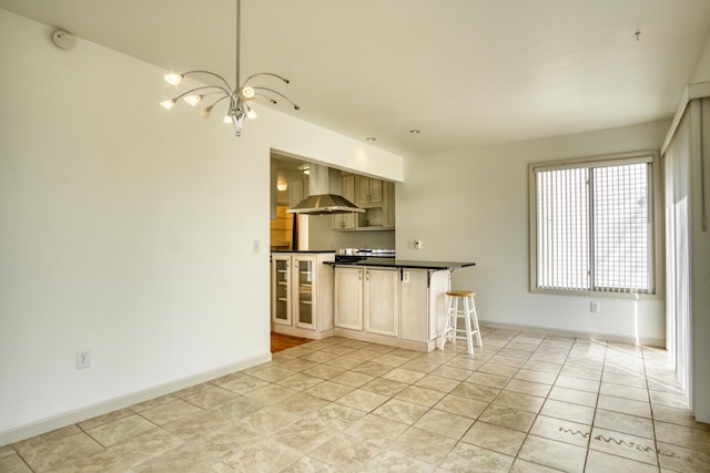 kitchen with dark countertops, an inviting chandelier, wall chimney exhaust hood, baseboards, and a kitchen bar