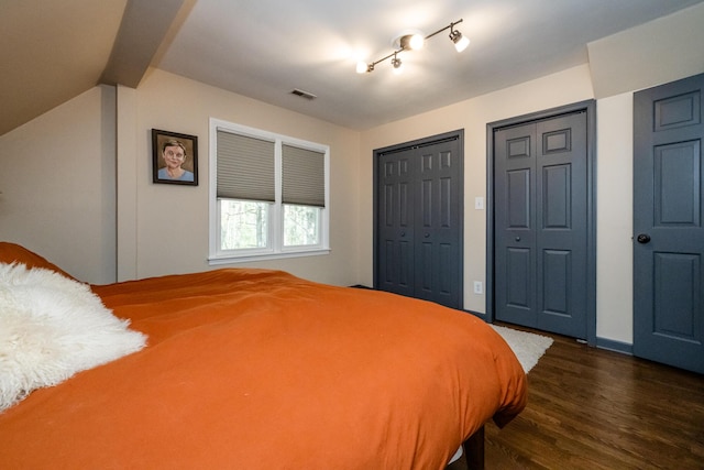 bedroom with visible vents, dark wood-style flooring, and two closets